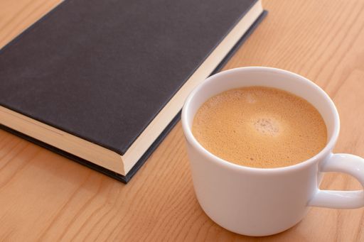 A closeup shot of a cup of coffee with notebook on the side on wooden table