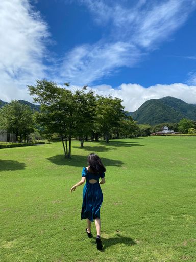 A vertical back view of a young female running in the field with trees against a blue cloudy sky
