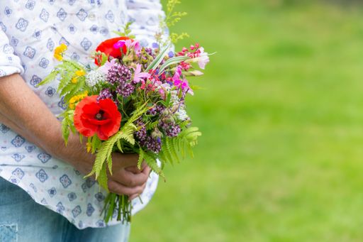 A selective focus shot of someone holding a bouquet of different flowers outdoors during daylight