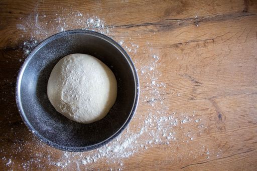 A top view of resting dough in a bowl on a wooden surface