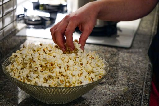 A closeup shot of a hand picking up freshly popped popcorn in a bowl