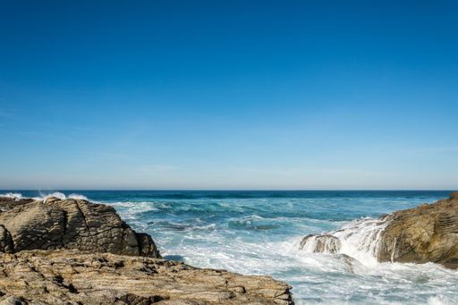 A beautiful shot of a seashore under a blue sky with waves crashing on the rocks