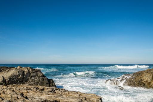 A beautiful shot of a seashore under a blue sky with waves crashing on the rocks