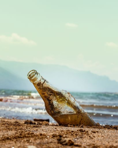 A vertical shot of a dirty bottle near the sea on a sunny day