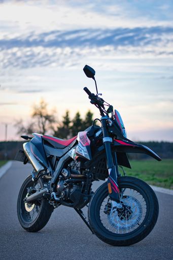 Aprilia SX 125 is standing with a blue sky on a road.