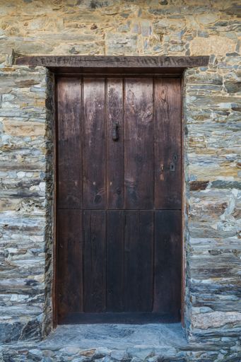 A vertical shot of an old wooden door in a stone wall