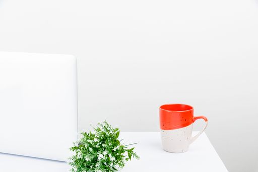 A tidy workspace with a laptop, coffe mug and small floral bouquet on a white background