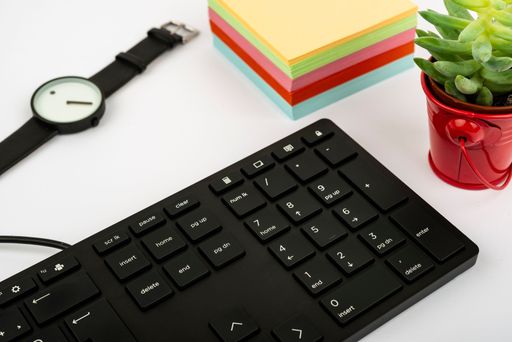 A closeup of a white desk with a computer keyboard, colorful notes and a watch,
