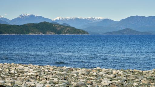 View from a rocky beach of the deep blue ocean, distant islands and snow covered mountains.