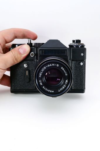A male hand holding a 35mm old SLR camera on a white isolated background