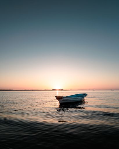 A vertical shot of a small boat floating on the water against a sunset sky