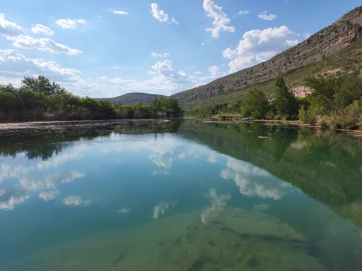 A high-angle shot of Devils river with trees, rocky mountains, and sky reflected in the water