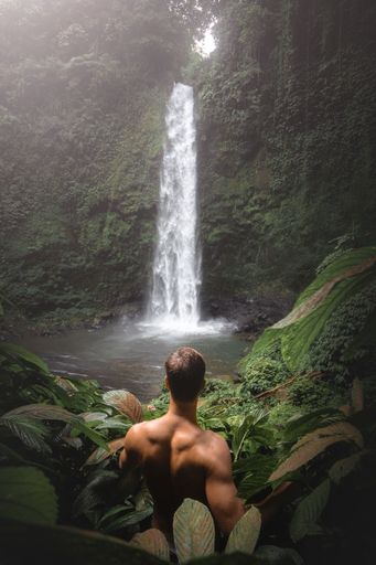 A vertical shot of a man in front of a waterfall in Bali, Indonesia