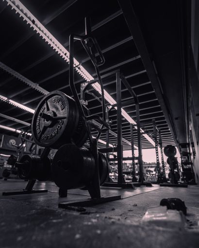A low-angle grayscale gym inside view with a barbell and other pieces of equipment around