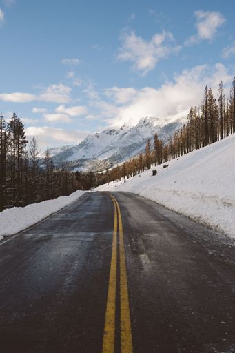 A vertical shot of clean asphalt mountain road with snow on both sides