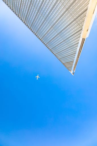 A low angle shot of a passenger plane flying in blue sky with building roof in the foreground