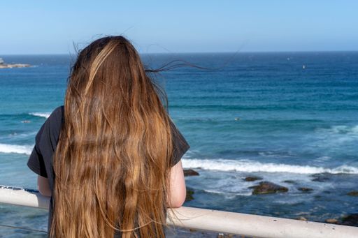 A back view of cute little girl with long hair watching the sea from the pier
