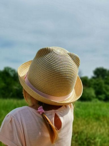 A vertical rear view of a girl with a straw hat