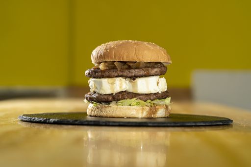A closeup shot of a beef burger with feta cheese on a black round board on a wooden table