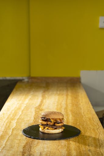 A vertical high angle shot of a burger on a black round board on a wooden table