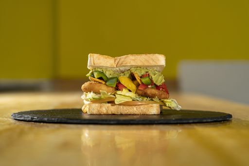 A closeup shot of a sandwich with toast bread and vegetables on a black round board on a wooden table