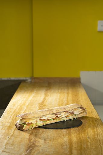 A vertical closeup shot of a baguette sandwich on a black round board on a wooden table