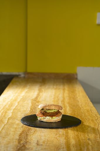 A vertical high angle shot of a beef burger on a black round board on a wooden table