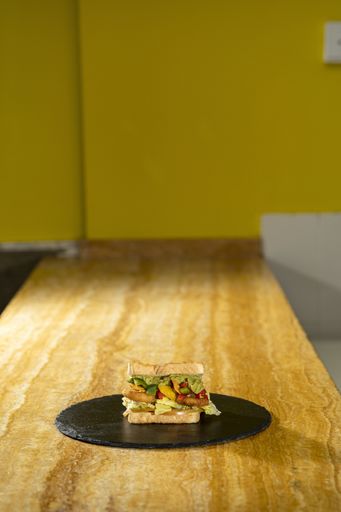 A vertical closeup shot of a sandwich with toast bread and vegetables on a black round board on a wooden table