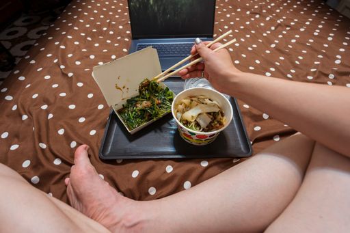 A high angle shot of a female eating Asian food and watching a movie on a laptop