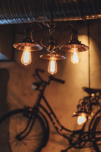 A vertical of a metal vintage chandelier with Edison bulbs and a blurred vision of a bicycle in a room