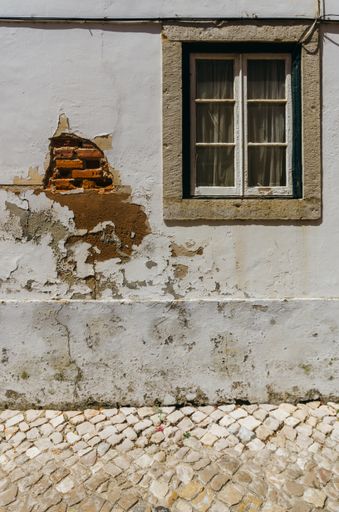 A vertical shot of the facade of an old house with a damaged wall and a window