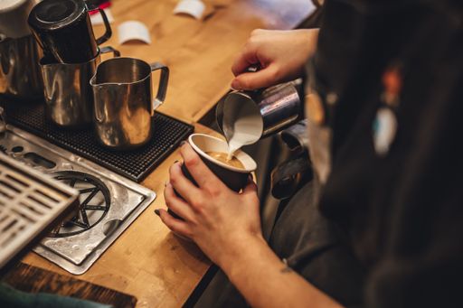 A female barista pouring milk to make a cup of cappuccino coffee in a coffee shop