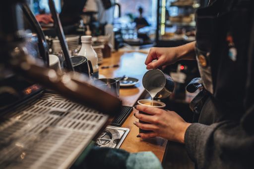 A female barista pouring the steamed milk into a shot of espresso to create latte art with froth