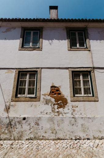A vertical low angle shot of the facade of an old house with a damaged wall
