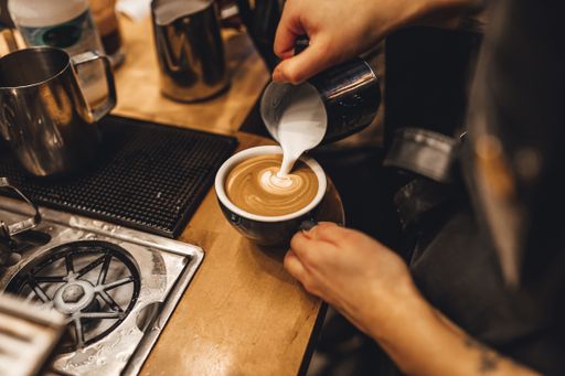 A female barista making latte art with by pouring steamed frothy milk into a shot of espresso