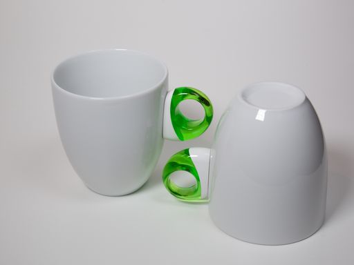 An isolated closeup shot of white ceramic mugs with green translucent handles on a white background