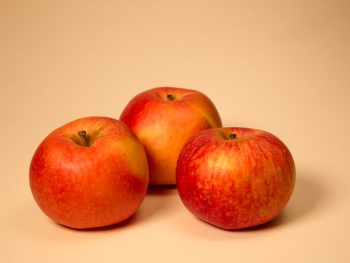 An isolated closeup shot of red and yellow apples on a beige background