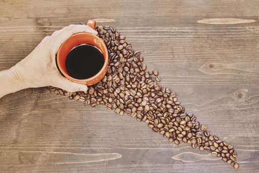 A top view of a person holding a cup of coffee with roasted coffee beans on the table