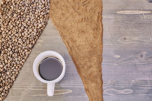 A top view of a cup of coffee on the table with roasted and ground coffee beans on it