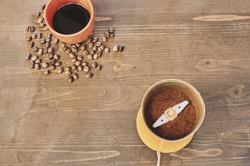 A top view of a coffee grinder with roasted beans and a cup of coffee on the table