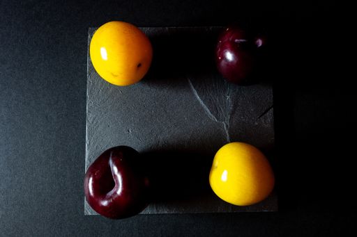 A top view of four red and yellow plums shaped like a square on a black background