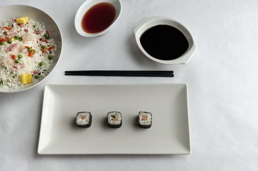 A top view of sushi on a plate on the table with sauces and cooked rice with vegetables and seafood
