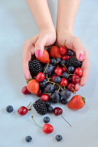 A vertical shot of a person holding different berries against a light blue background