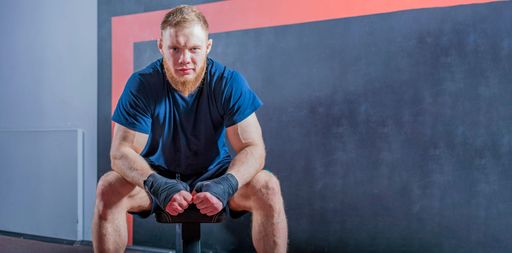 Strong muscular mixed martial arts fighter sits on couch. His hands are wrapped in elastic bandage for open fisticuffs. Look at camera.