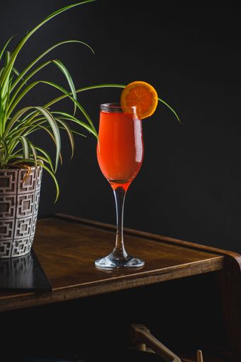 A vertical shot of a glass of orange cocktail on a wooden table