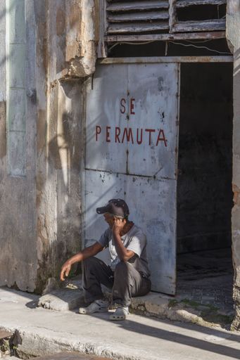 A vertical shot of a poor man sitting at the door of his house with the text exchange
