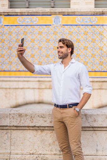 Young caucasian man with blond hair dressed in casual clothes taking a selfie with his cell phone in the city center of Valencia at Mercado Central.