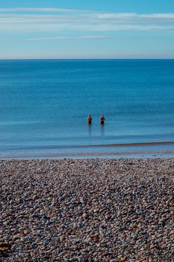 A beautiful view of a rocky beach with two swimmers in the sea on a sunny day