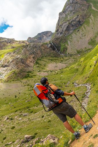 A young man on the mountain trekking with his son in the backpack