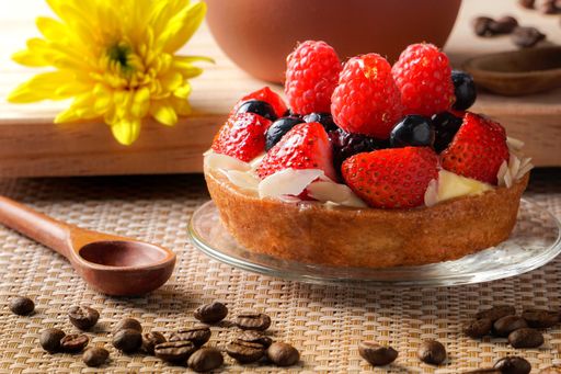 A small whole cheesecake with strawberry and raspberry served with a wooden spoon